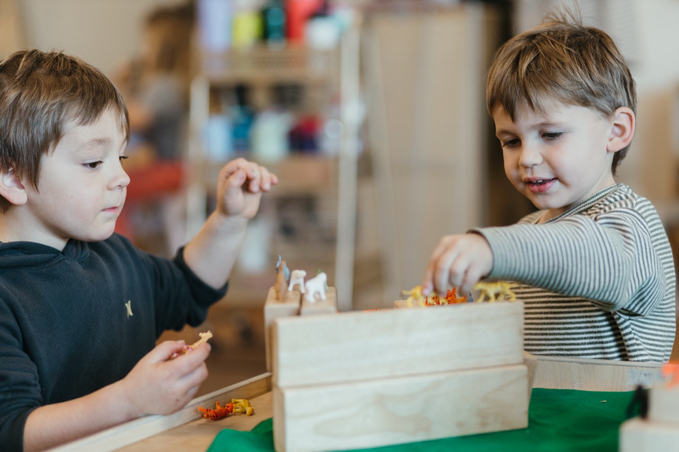 Two young boys playing with wooden blocks and small animal figures at a table in the Wonder classroom